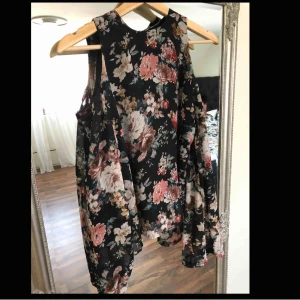  - Blommig blus med öppna axlar. Dragkedja bak.