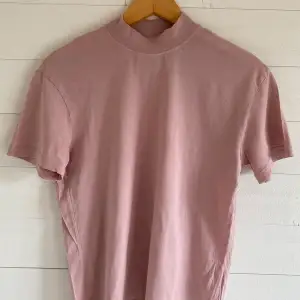 En t-shirt från & Other Stories i en rosa/mauve ton. Har en turtle neck-krage. Originalpris: 300 kr