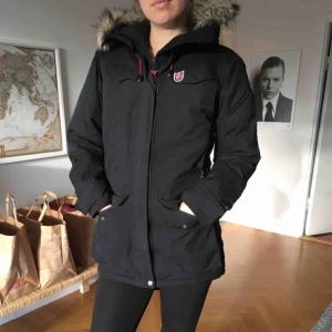  - Varm, svart fjällrävenjacka med röda detaljer. Bra skick förutom att höger arm har jag en gång gått emot en varm kabin. Syns knappt då det är på insida ärm. Storlek XS men är mer som en S. Ev. frakt tillkommer.