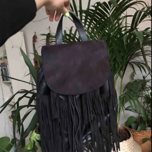  - Svart ryggsäck med fransar framtill. Stängs genom att dra åt snöre och stänga med locket. Använd men fortfarande i bra skick. 