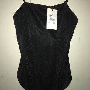 Glittrig body storlek xs - Svart glittrig body med reglerbara band. Lappen kvar, aldrig använd.