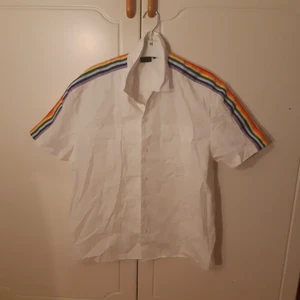 Regnbågs-skjorta - Kortärmad skjorta med regnbågar på ärmarna. Fint skick! Märkt S i herrstorlek men tycker den känns större än så. Priset är exklusive frakt, kan både mötas upp i Göteborg och skicka! Obs, katt finns i hemmet!