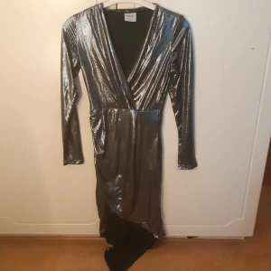 Silver-klänning - Silver/metallic-klänning! "Omlott" vid både urringning och där nere, längre bak än fram! Märkt S men passar troligen en M också. Fint skick! Priset är exklusive frakt, kan både mötas upp i Göteborg och skicka. Obs katt finns i hemmet!
