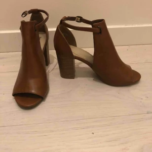  - Skor, storlek 37 i äkta brunt läder. Köpta på din sko och är sparsamt använda. Skorna har öppna tår och en bredare klack. 