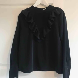  - Storlek 38, Svart blus med volang från H&M, nyskick