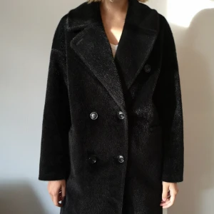  - Svart kappa i fuskpäls från NA-KD i stl 38. Sparsamt använd!  Köpare betalar frakt / kan mötas upp i Sthlm. 