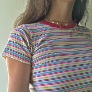 Färgglad Randig Babytee Croptop - Asgullig liten babytee med färgglada ränder😋 Har två knappar på ena sidan av kragen som går att knäppa upp💓 Barnstorlek men passar XS!🤩  Frakt 22kr