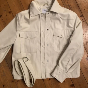 Vit snygg höst-jacka   - Hej! Säljer en vit jacka i läderimitation från Berschka- helt nyskick- ej använd! Säljes pga retur gått ut så gick ej att lämna tillbaka. Snygg modern jacka, något oversize modell. Till jackan kommer ett skärp med silverspänne/ring som man kan knyta i midjan, man kan också välja ha den utan så får jackan en mer rak siluett. Perfekt jacka för sen-sommar och höst, man får plats med varm tröja under. Köparen betalar frakt, men kan också hämtas i sthlm. Hör av er om ni har frågor!  /I 