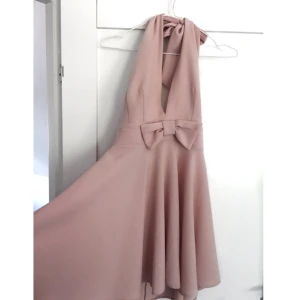  - Klänning från Nelly med fin urringning. Använd en gång och är i nyskick. Försluts med dragkedja på baksidan och knytet i nacken gör klänningen justerbar i storleken och kan därmed passa dig med storlek 36-40.