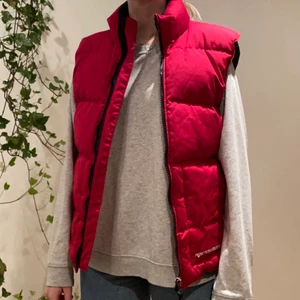 Peak Performance väst strl: XS - En röd, varm väst från Peak Performance. Har två ”dubbelfickor” framtill där den innersta är öppen och den yttersta har dragkedja, samt en innerficka med dragkedja. Har varit i en källare ett litet tag och har därför en svag lukt av ”källare”. Men har vädrats utomhus ett tag nu, därför luktar den inte speciellt mycket.  Material: Bomull, polyester och polyamid Material fyllning: 80% dum, 20% fjäder