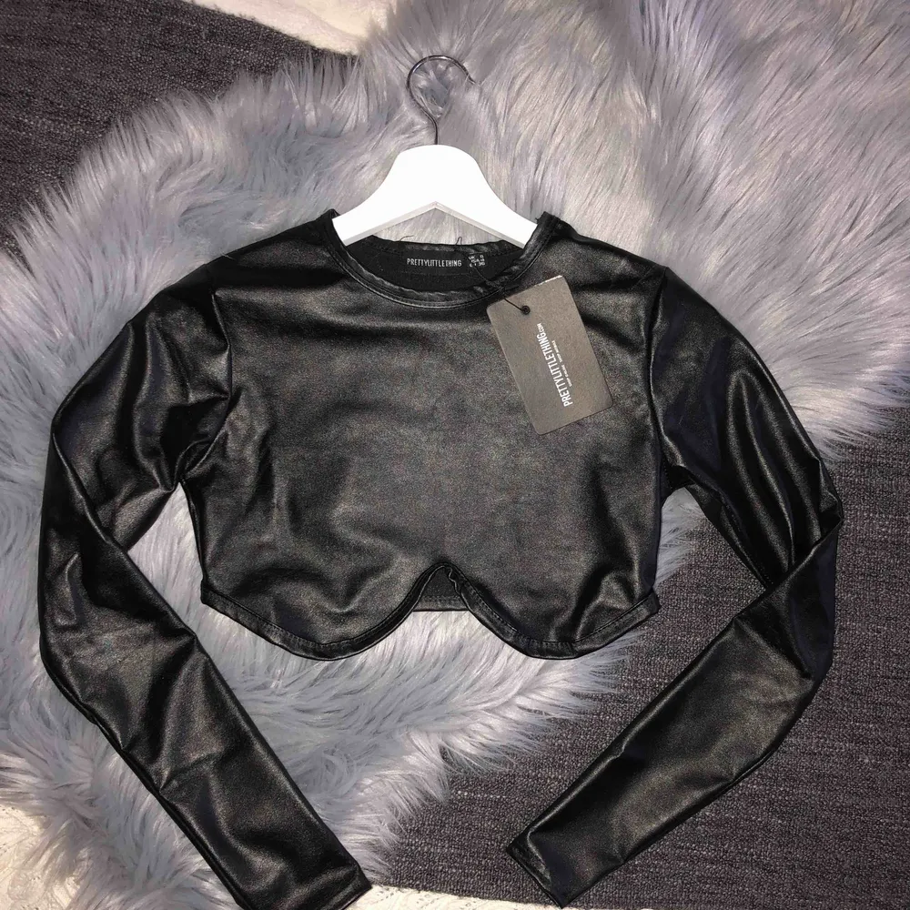 Svart crop top i läderimitation. Beställd från Pretty Little Things nyligen, aldrig använd. Storlek UK 8/ EU 36, men liten i storleken så passar bra som en 34.  Frakt ingår inte i priset. Kan dock mötas upp i Stockholm kostnadsfritt!. Toppar.