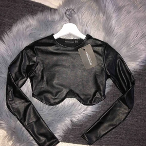 - Svart crop top i läderimitation. Beställd från Pretty Little Things nyligen, aldrig använd. Storlek UK 8/ EU 36, men liten i storleken så passar bra som en 34.  Frakt ingår inte i priset. Kan dock mötas upp i Stockholm kostnadsfritt!