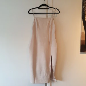 Mocka klänning med slit - Helt ny, oanvänd beige mocka klänning med hög slit. Denna klänning går till knäna ungefär (midi), låg rygg och hög slit. Axelbanden går att justera. Superfin och formad klänning. Köpt i storlek 10 uk ( EU 38).
