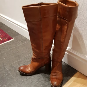Bruna skinnstövlar stl 36 - Stövlarna har höga skaft och remmar vid foten. Skinnet har snygg patina och de är sköna att gå i eftersom klacken är bred. De kan hämtas på Södermalm eller på annan plats i Stockholm. Annars betalar du frakten
