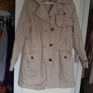 Trenchcoat  - Oanvänd skick men tyvärr inget skärp till , formar sig snyggt med något utsvängd nederdel 