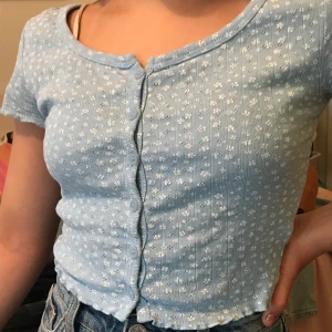 Blå croppad top med vita blommor på - En blå top med vita blommor som passar xxs-s. Använd en gång. 130 kr inkl frakt.