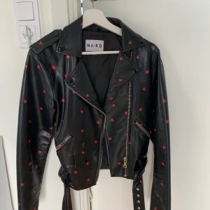 Skinnjacka från nakd med röda hjärtan  - En jättefin skinnjacka med hjärtan som tyvärr inte kommer till användning tillräckligt mycket. Jackan är i xs men passar en s. Frakten ingår i priset!