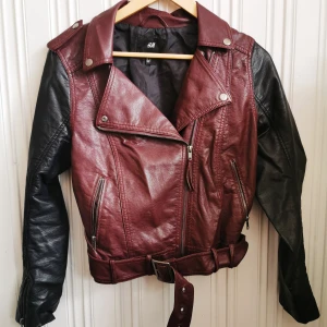 Skinnjacka från HM Stl. 40  - Cool skinnjacka i svart och vinröd med detaljer. Bra passform och den är reglerbar vid handlederna. Skönt material och den ser som ny ut. 