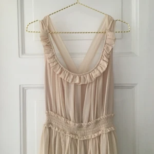  - Off-white/beige långklänning från Nelly. Aldrig använd, strl 36. Har innertyg och öppen rygg med skira band bak.   Kan mötas upp i centrala Sthlm eller skicka - köparen betalar frakt