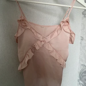 H&M linne storlek s - Ett fint babyrosa linne med volanger. Den har skjusterbara band så att den passar bra på kroppen. Har använt den några gånger förra sommaren men kom inte till använding iår. Den är som ny, har dock klippt av lappar på ryggen för att de kliade. 