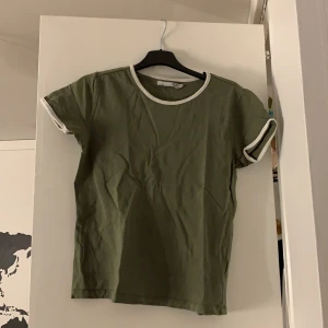 Fin mörkgrön t-shirt me vita kanter - Militärgrön/ mörkgrön t-shirt me vita kanter vid armarna och halsen, knappt använd i bra skick.