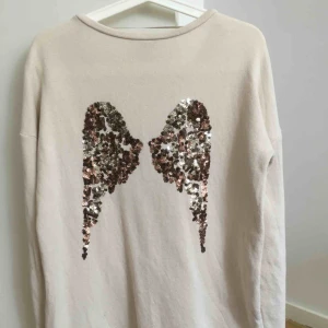  - Beige tröja med råa kanter från Gina Tricot. Vingar av paljetter på ryggen. Väldigt bra skick, knappt använd!  
