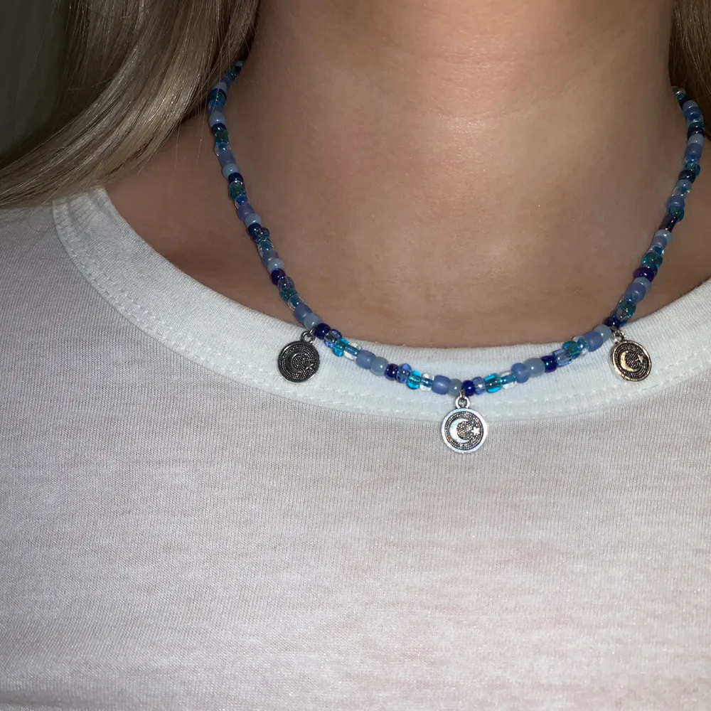Blått pärlhalsband med 🌙-berlocker🦋💙🤍🥺 halsbandet försluts med lås och tråden är elastisk . Accessoarer.