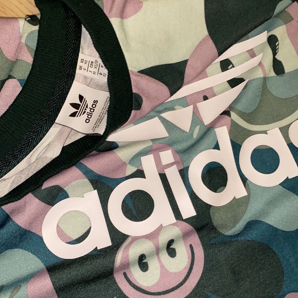 Sportig och cool mönstrad adidas t-shirt. 💚💙🖤💜🤍 Med stort adidastryck i vitt, mönstrad med blommor smileys och typ kamouflage, svart krage, och passar bra till träning, men kan även användas till vardags. 100% polyester. Mycket bra skick då den endast är använt fåtal gånger. XS men sitter lite oversized och snyggt på mig som är en XS/S. Funkar somsagt bra till träning och lek. DM vid intresse/fler frågor/ fler bilder.❣️(Det kan du göra här under för det står ”kontakta”) Avhämtning på Södermalm eller frakt till självkostnadspris.:). T-shirts.