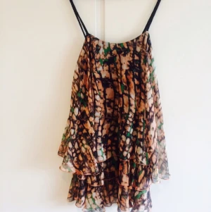  - Mönstrad klänning i volanger med underkjol i använt skick, men fortfarande hel och ren! Flätade axelband och storlek 38/40 skulle jag säga. Resår i ryggen håller den på plats! Hör av er om ni har några frågor! 😊