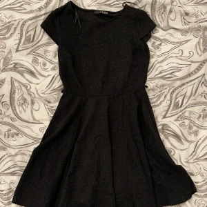 Svart klänning  - Superskönt tyg, fint mönster på. Säljer för 89kr. Toppskick! Använd en gång. Storlek S (passar M/XS beroende på passform du vill ha) tajt runt midjan så den formar kroppen fint. 