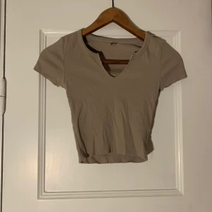 Beige croppad t-shirt  - Beige croppad ribbad tshirt med en liten v-ringning. Strl S
