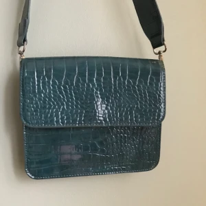 Grön axelremsväska från Hvisk  - Säljer denna väska från Hvisk pga felköp. Jättefin mörkgrön färg åt det blåa hållet. Perfekt vårväska!! Nypris 749 kr. Gratis frakt. Buda i kommentarerna. 💚🩱🩴🧤🐊🦚 