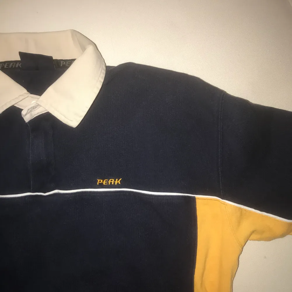Pikétröja från peak performance i färgerna marinblå och gul, köpt på secondhand, men har aldrig kommit till användning . T-shirts.