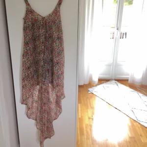  - Sommarklänning i mycket bra skick, lång baktill och kort framtill. Svart underkjol. 100% polyester. Blommig.
