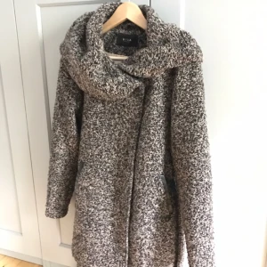  - Mysig jacka från Vila.  Stor krage, stängs med knappar/skärp.   Är "stickat" material, lite noppig men inget som stör pga strukturen som redan finns i tyget. 