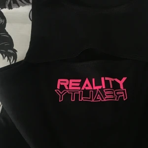 Body - Stretchig body med string. Den är öppen vid nyckelbenen vilket ger den en festlig look. Det står reality i rosa text som är reflekterande, as coolt! Frakten är inräknad i priset🥰