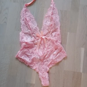  - Oanvänd spetsbody med vacker rosa färg! (endast tvättad) Rosett fram och bak. String/cheeky och knyte bakom nacken. Superlyxig och sexig. 