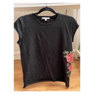 Therese Lindgren Felicia Tee - Felicia Tee från Thereses Lindgrens kollektion för NA-KD med en broderad ros på vänstra sidan. Fint skick :)