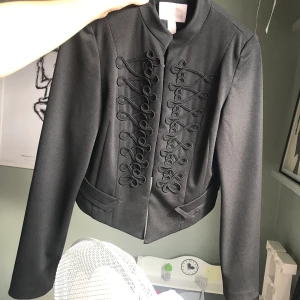 Svart kavaj med snygga detaljer - Svart kavaj med snygga detaljer från Forever21. Kortare baktill. Lite stretchigt material. Nyskick! Betalning med swish. Frakt ca 50kr