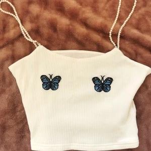 Crop top med fjärilar - Säljer denna fina topp pga den är för stor för mig. Storlek: S, men skulle säga att den passar M mer. Avtagbara axelband med pärlor på, så att man kan tvätta den utan att förstöra pärlorna 🌹 Köpare står för frakt! 💕