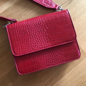 Röd axelbandsväska från Gina tricot - Väska från ginatricot, köpt förra sommaren men har knappt kommit till användning. Väskan är i fint skick, den går att stänga med magnet och vill man ha något annat band till så är det avtagbart. 🌸 möts upp i Stockholm eller postar (frakt 40kr)🌸