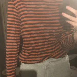 monki randig tröja  - orange och svart/mörkgrå långärmad randig tröja. köpt på monki för många år sedan. använd en del men i väldigt bra skick, tyget är väldigt mjukt. köparen står för frakt