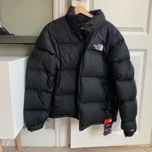 NY! Svart The North Face Iconic Nuptse stl.M - Helt ny ”mens” dunjacka från The North Face köpt i butik på Kungsgatan, Stockholm. Säljer pga. har ångrat mig och öppet köp har utgått. Passar mig jättebra som normalt har storlek S och den sitter lite,sådär snyggt oversize. Ord.pris: 2799kr . Köpare står för frakt.