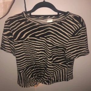 Halvt kroppad, zebramönstrad tisha med knytdetalj - H&M ~ lite halvt kroppad t shirt med en slags knytdetalj ~ Aldrig använd pga snäppet för liten då jag köpte fel storlek ~ Hämtas i Norrköping eller så står du för frakten🌟 Passar en M som den ska dvs lite kroppad och förmodligen en S lite mer som en vanlig tisha 