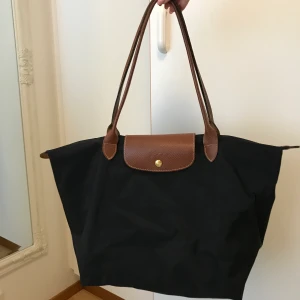 Longchamp Väska Svart - Longchamp väska i svart färg. Fint skick. Storlek Medium Höjd 28cm Bredd 30cm-47cm. Köparen står för frakt. 