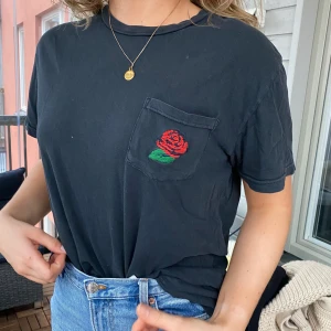 Svart T-shirt med broderad ros - En T-shirt köpt på Urban Outfitters för nåt år sen som inte kommer till användning