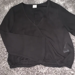 En fin svart lite kortare blus, väldigt tunn. - Den är tunn och luftig, längst ner i ärmarna är den lite mer vid.