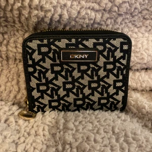 DKNY Plånbok - En supersnygg plånbok i mörk marinblå around logo, från DKNY NEW YORK. Den är i mycket gott bruksskick, bruksslitage särskilt metalldelar, OBS! plasten borta från 'körkortsfacket'. OBS! Se/zooma alla bilderna. 