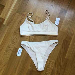 Beige bikini från NA-KD. Oanvänd med prislappar kvar samt skyddsplasten kvar i trosan. Storlek S i underdel och M i överdel. Överdelen har justerbara band.   Skickas alt. möts upp i Stockholmsområdet. 