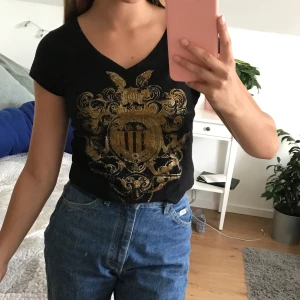 T-shirt  - Svart t-shirt med guldigt märke. 🖤🦁💛